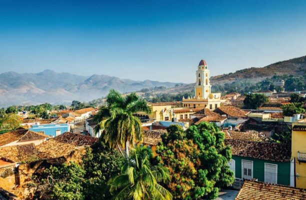 Panoramic view over the city of Trinidad, Cuba with mountains in the background and a blue sky. The bell tower belongs to the Iglesia y Convento de San Francisco.