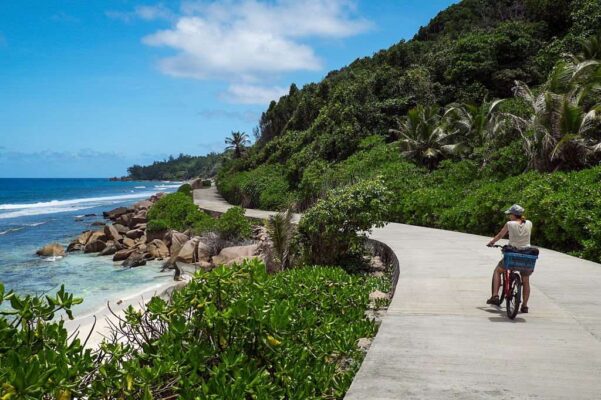 Woman cycling along the ocean on the east side of La Digue Island, Seychelles.