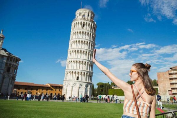 A woman is gesturing with her hands in front of the Leaning Tower of Pisa